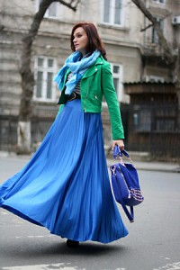 Модель в длинной синей юбке, зеленой кожаной куртке с большой сумкой синего цвета в руке