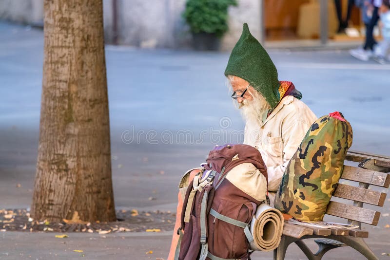 A senior man backpacker sitting on a square bench, is writing down notes on a notepad wearing eyeglasses and a gnome wool hat. Ancona, Italy - September 27th royalty free stock photography