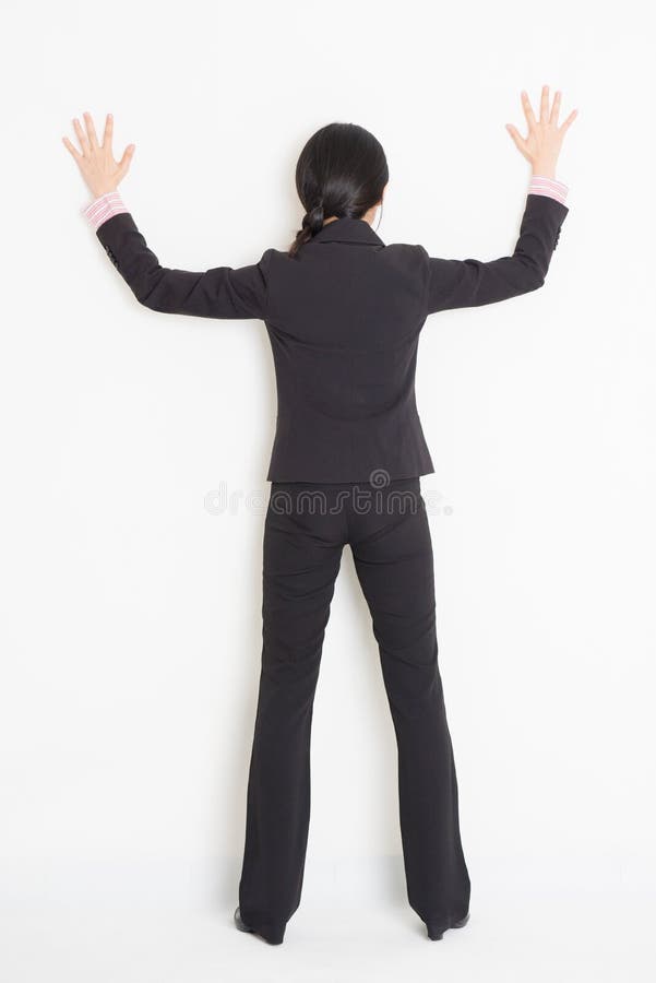 Asian businesswoman banging on wall. Full body back view of young Asian businesswoman in formalwear banging on wall, standing on plain background royalty free stock images