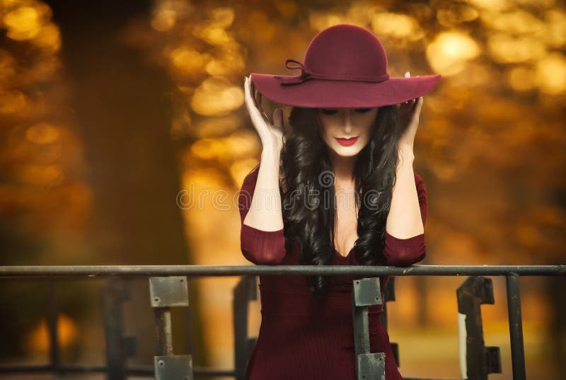 Attractive young woman with burgundy colored large hat in autumnal fashion shot. Beautiful mysterious lady covering the face stock image