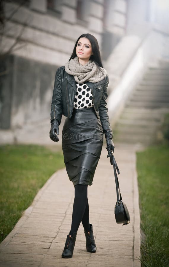 Attractive young woman in a winter fashion shot. Beautiful fashionable young girl in black leather waking on avenue. Elegant woman. Attractive young woman in a royalty free stock photos
