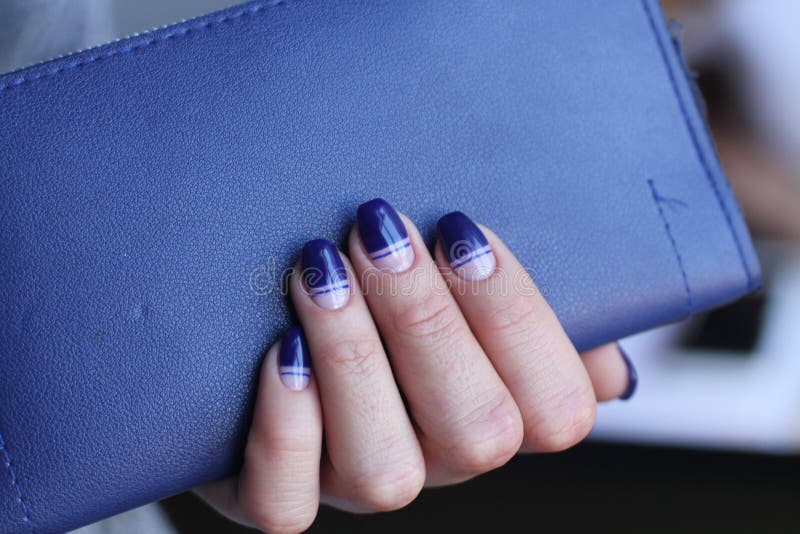 Beautiful female hand with manicure holds leather clutch. Dark blue nail polish with creative design. stock photography