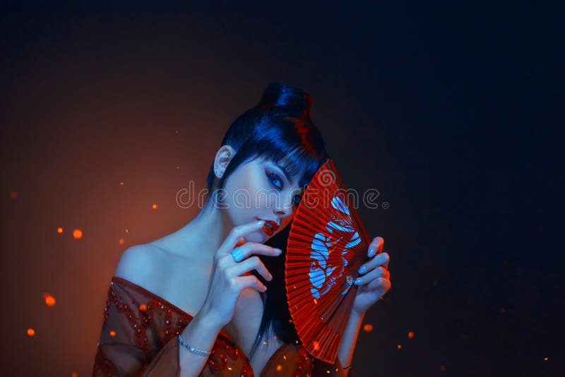 A beautiful geisha with blue long hair and a bang is looking in soul. red make up, lips, long dress with open shoders. And deep neckline. holding scarlet fan in royalty free stock images