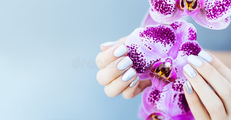 Beautiful hand with perfect nail pink manicure and purple orchid flower. on light blue background. stock photos