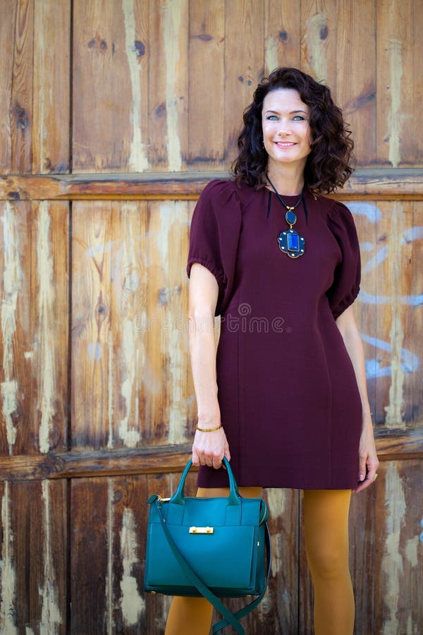 Beautiful middle-aged woman in a burgundy dress and green handbag stock photo