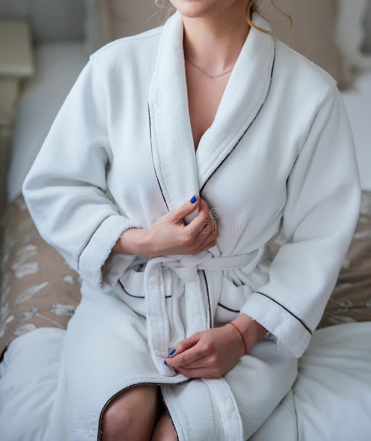 Beautiful slim girl in white robe after shower sitting on bed. royalty free stock images