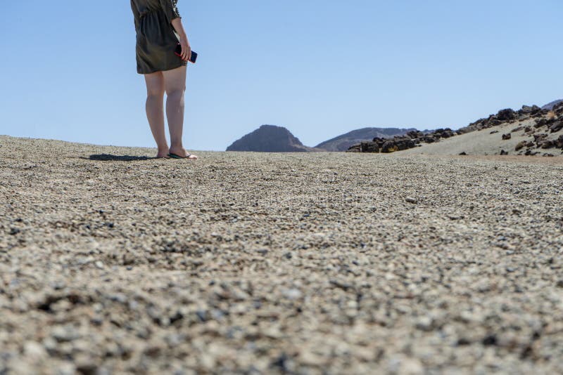 Blond hair teen in relaxing mood at remote lunar, volcanic and arid desert. Back of Spiritual woman in green dress walking alone. On volcano path with white royalty free stock image
