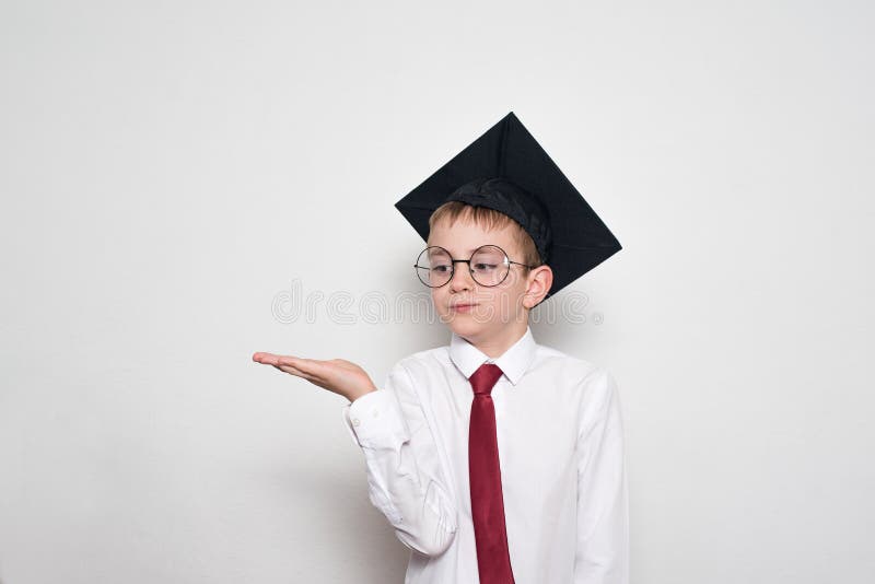 Boy in a square academic hat and glasses holds his palm up. School concept. White background.  stock photography
