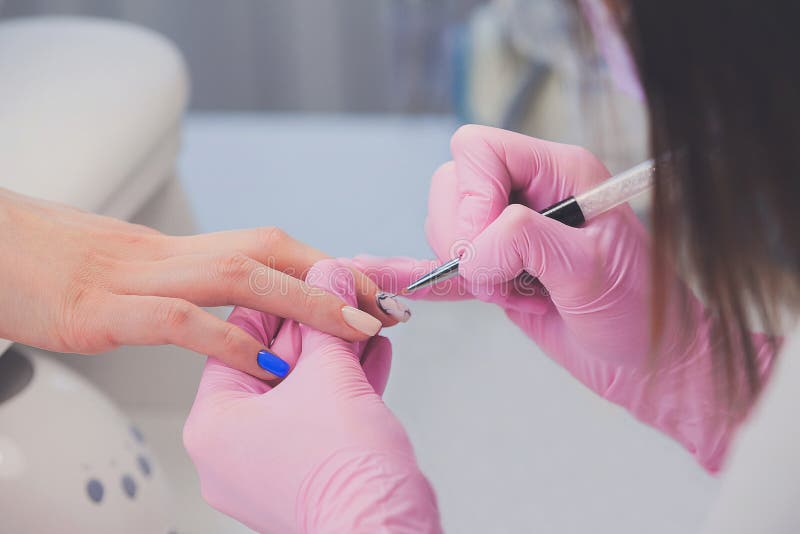Closeup shot of manicurist in pink rubber gloves paints pattern with brush on female nails stock photography