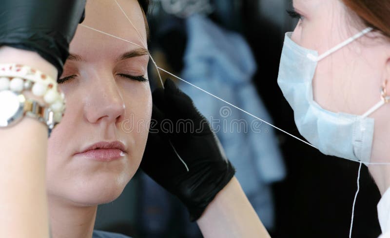 Cosmetologist performs the procedure of correction eyebrow threading. Side view. Cosmetologist performs the procedure of correction eyebrow threading royalty free stock photos