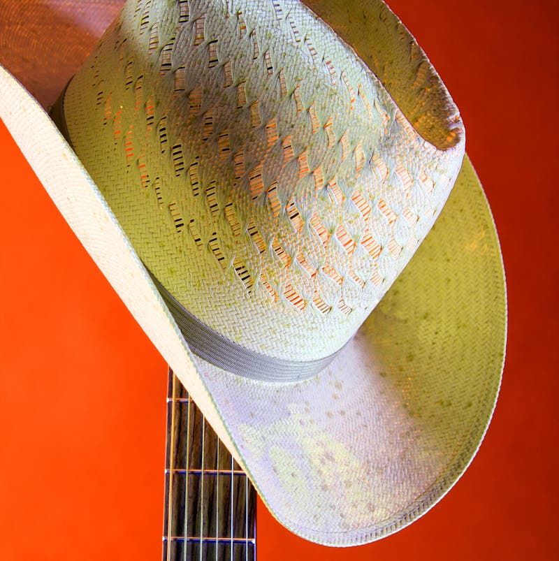 Country Western Hat On Orange. A country western hat on a guitar neck isolated against an orange background in the square format stock photo