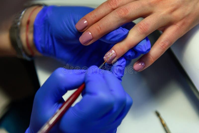 Covering the nails with gel polish, drawing picture on the nail plate. Manicurist in blue gloves apply varnish with a thin brush. royalty free stock image