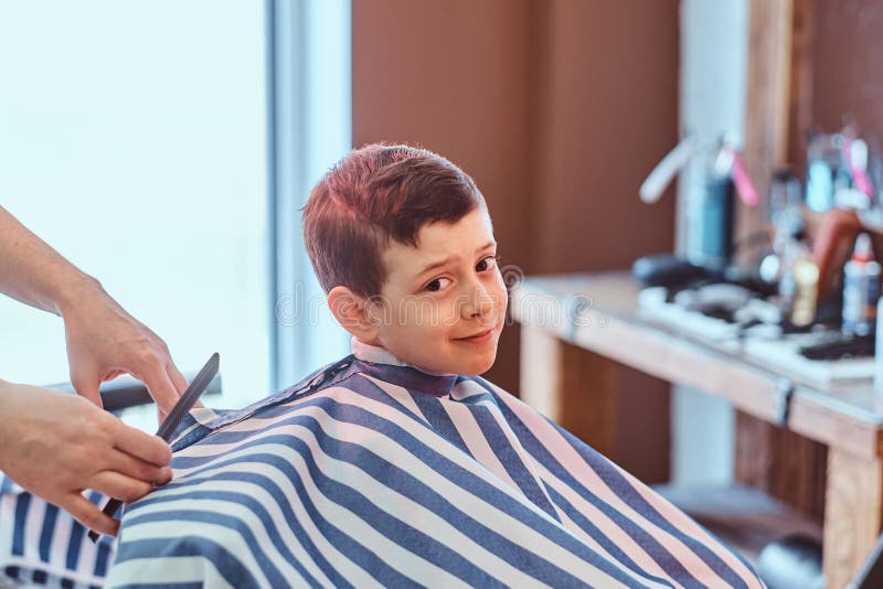 Cute little child is getting trendy haircut from barber at busy barbershop.  royalty free stock photos