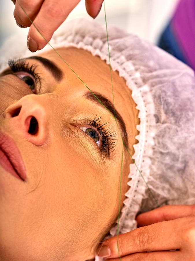 Eyebrow threading of woman middle-aged in spa salon. Master corrects of eyebrows gives shape and thread plucks eyebrows Tweezing eyebrow of 40s old female royalty free stock photos