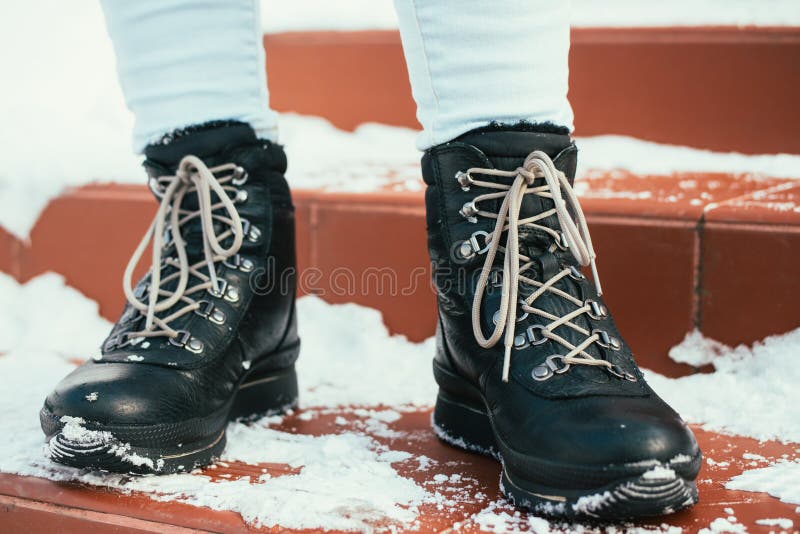 Female feet in winter boots with laces are on the stairs in the. Female feet in winter black boots with laces are on the red stairs in the snow royalty free stock image
