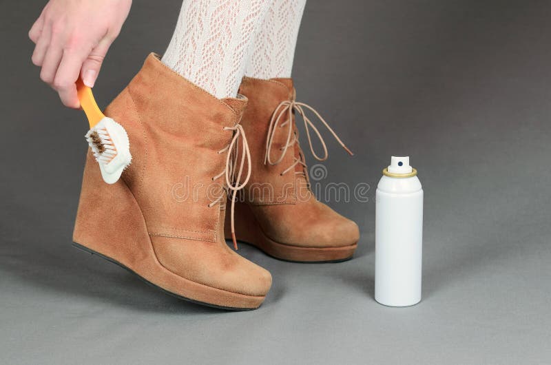Female legs in brown suede boots on a gray background. Woman cleaning her suede shoes.  stock photo