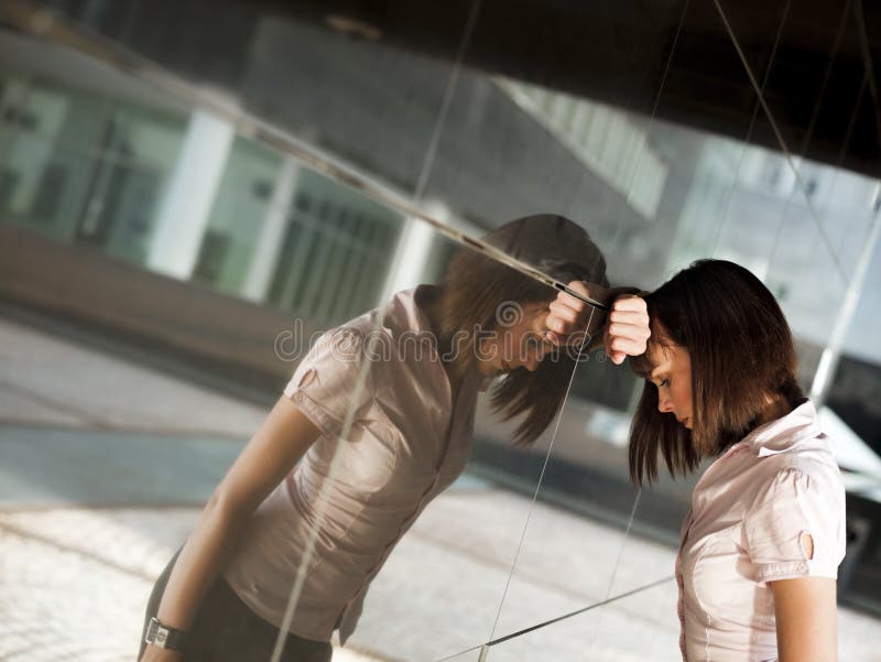 Frustrated woman banging head against wall. Sad caucasian business woman banging her head against a wall out of office building. Reflection on wall stock images