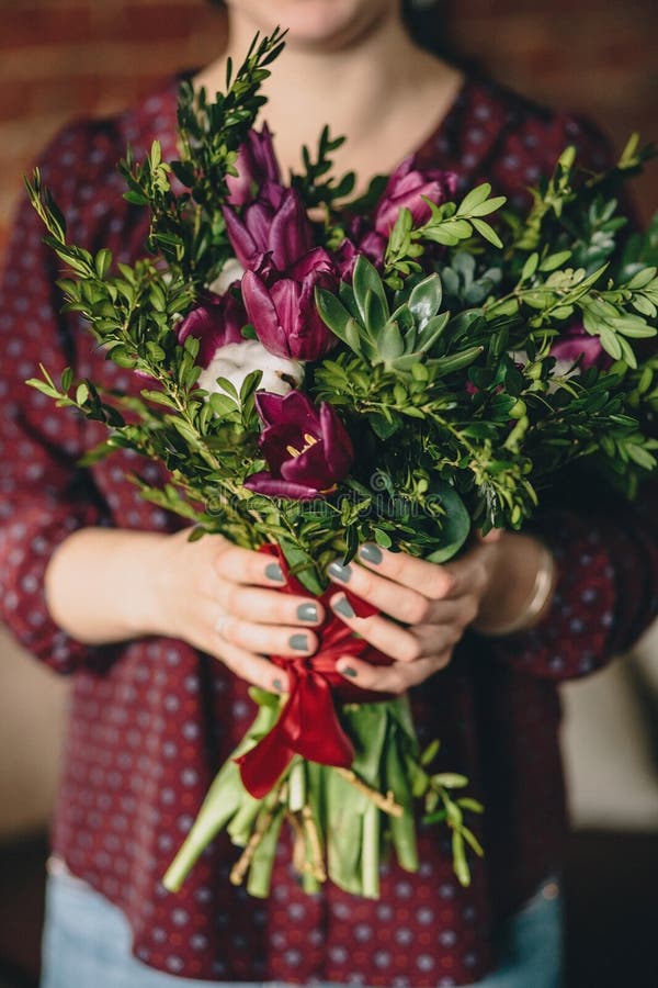 A girl in a burgundy blouse holds a bouquet of tulips, boxwood and plants with a manicure stock photos