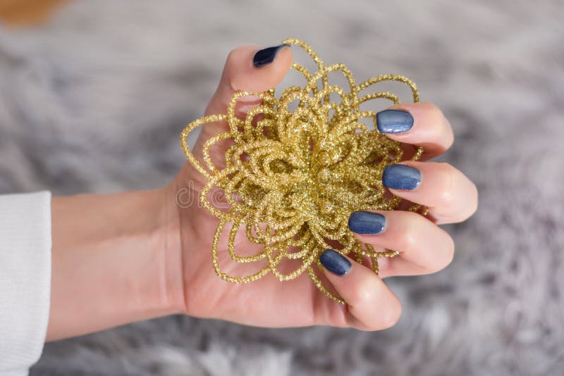 Girl with navy blue manicure on finger nails holding decorative golden flower stock image