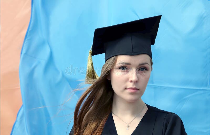 Graduate attractive young girl with red hair dressed in black mantle and square academic before flag stock photos