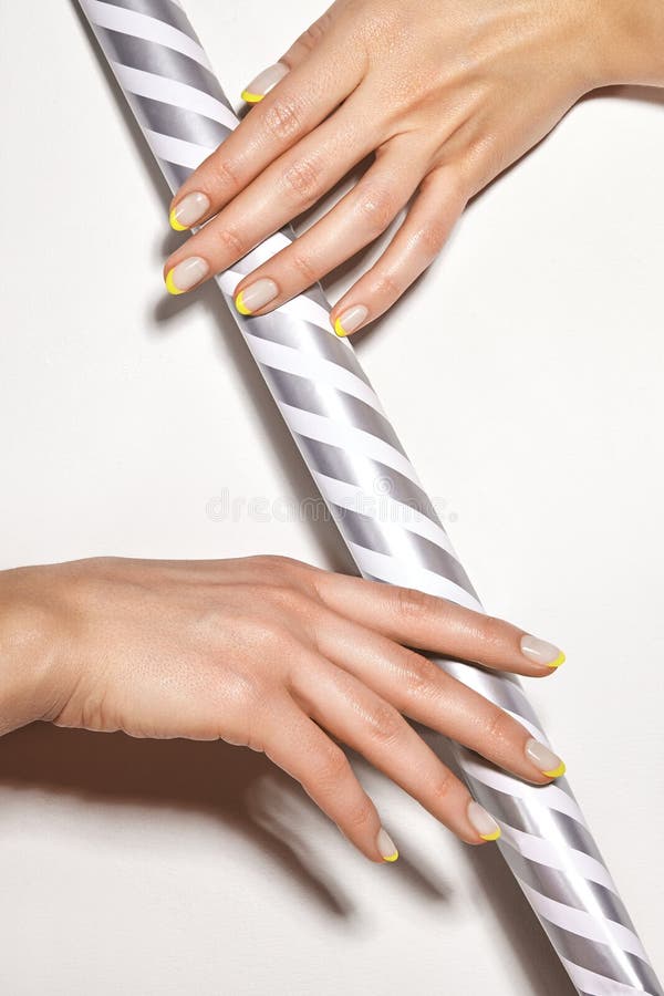 Hands with bright yellow french manicure. Nails art design. Close-up of hands with trendy neon nails on striped print stock photo