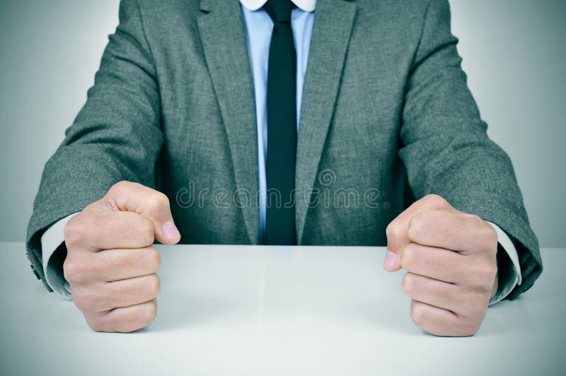 Man in suit banging his fists on a desk. Closeup of a young caucasian man wearing a gray suit banging his fists on his office desk royalty free stock image