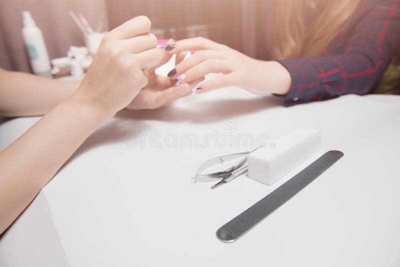 Manicure at beauty salon. Applying gel coating to girl with long hair. Close-up, warm lighting. Focus on tools royalty free stock image