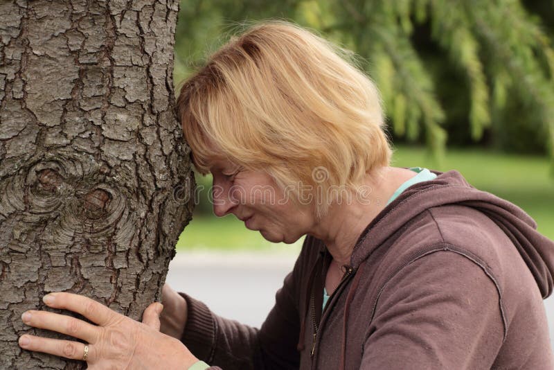 Mature woman banging head against tree. A mature woman banging her head against a tree trunk stock photo