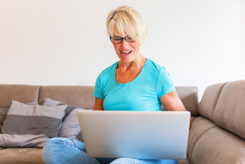 Mature woman sits who is rejoicing with raised hands in front of a laptop royalty free stock photos