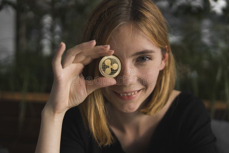 A nice girl is attaching a gold ripple coin to her eye. Bitcoins, crypto currency, electronic money. Woman sitting in. Cafe holding bitcoin in front eye royalty free stock photo