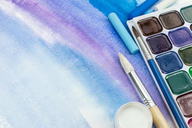 paints palette with paintbrushes and pastel crayons on blue watercolor background royalty free stock photography