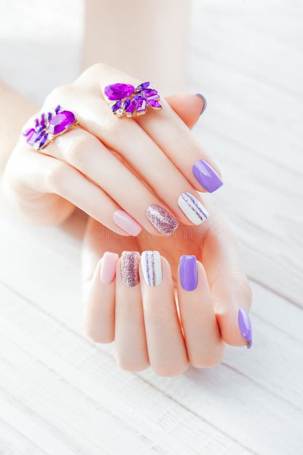 Pastel manicure with earrings on white background. Combination of purple, white, pink colors and sparkles. stock photos