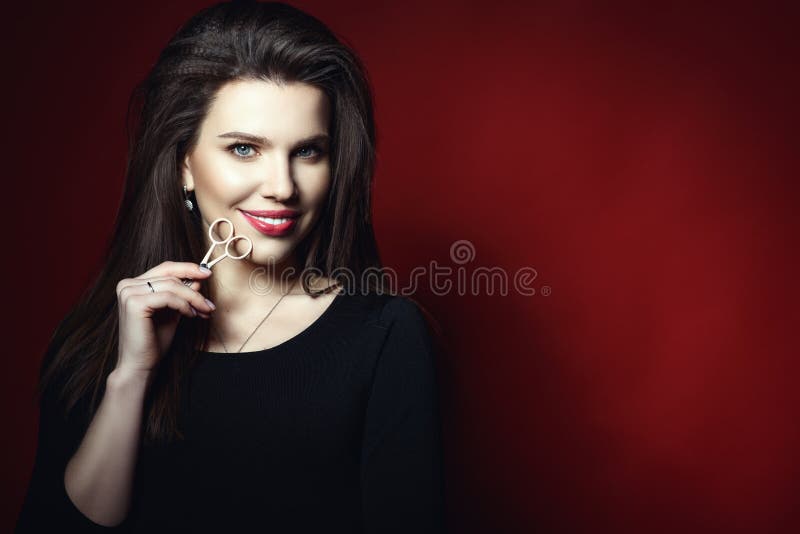 Portrait of beautiful smiling eyebrow master holding eyebrow scissors at her face. Isolated on red background. Beauty sphere concept. Studio shot. Text space royalty free stock photo