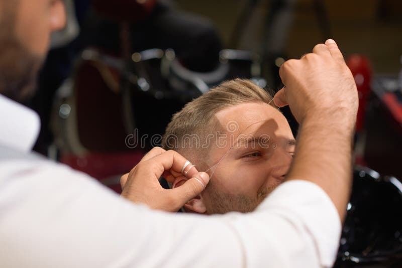 Barber doing threading procedure of eyebrows in barbershop royalty free stock photo