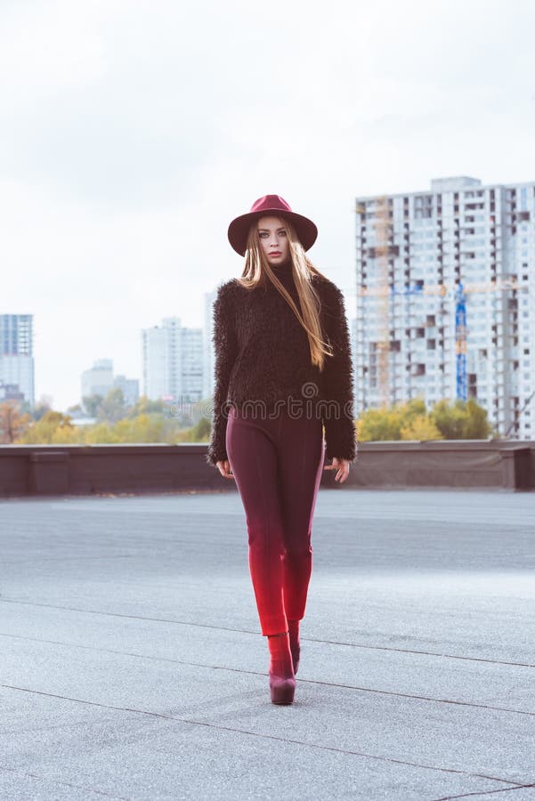 Stylish woman in burgundy hat and autumn outfit walking on a royalty free stock photography