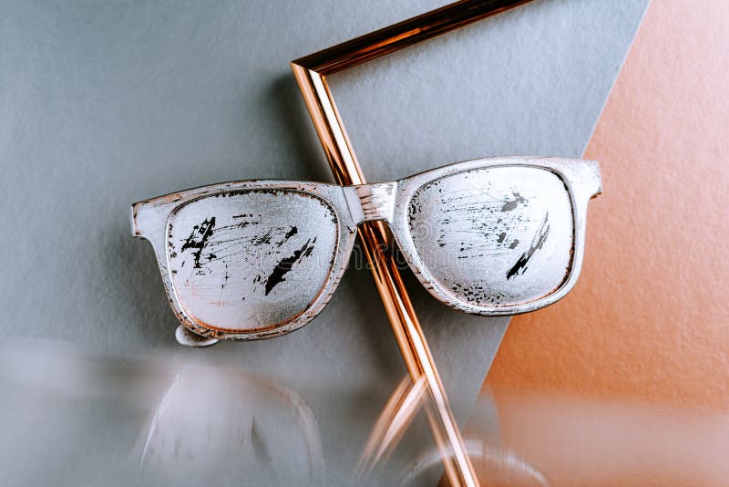Summer glasses silver color with scratches on a gray copper paper geometric background with a metal gold frame and reflection in. The mirror stock image