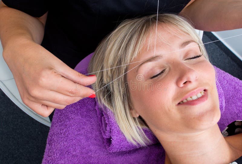 Threading hair removal. Beautician makes threading hair removal procedure to blond woman in salon royalty free stock image