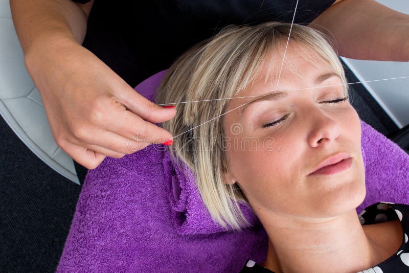 Threading hair removal. Beautician makes threading hair removal procedure to blond woman in salon stock photos