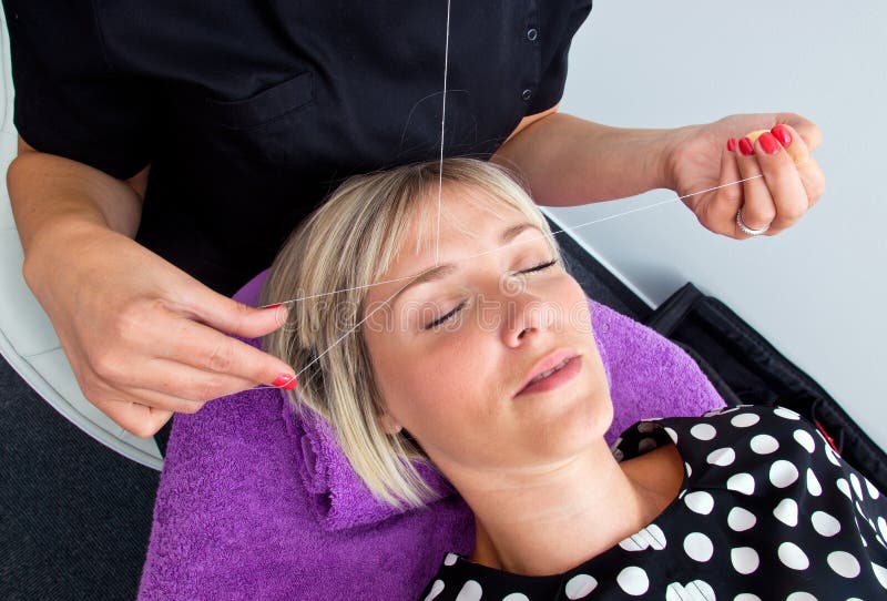 Threading hair removal. Beautician makes threading hair removal procedure to blond woman in salon royalty free stock photo