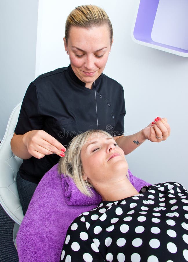 Threading hair removal. Beautician makes threading hair removal procedure to blond women in salon royalty free stock photo