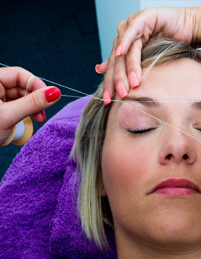 Threading hair removal procedure. Beautician makes threading hair removal procedure to blond woman in salon royalty free stock photo