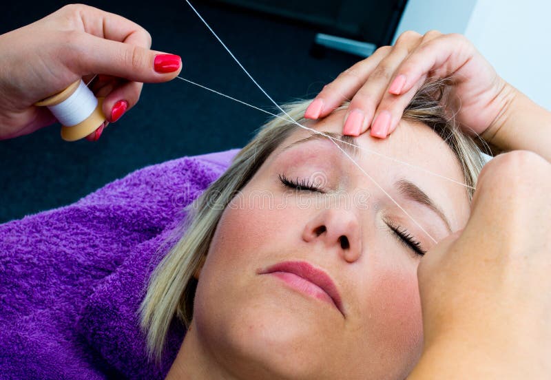 Threading hair removal procedure. Beautician makes threading hair removal procedure to blond woman in salon royalty free stock photos