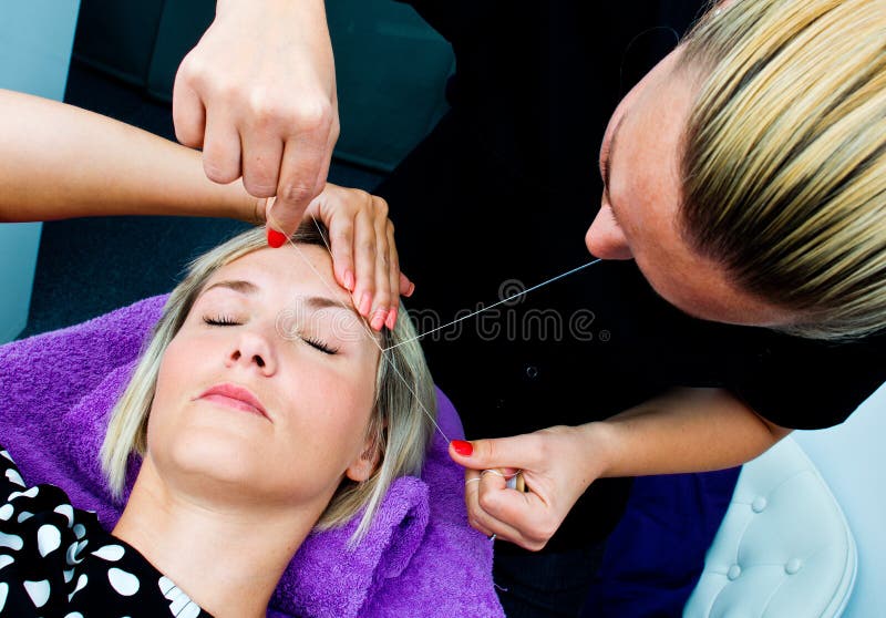 Threading hair removal procedure. Beautician makes threading hair removal procedure to blond women in salon royalty free stock photos