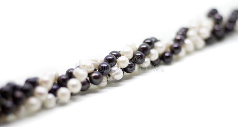 Two strands of white and black pearls intertwined on white background. Two strands of white baroque and black pearls intertwined on white background royalty free stock image