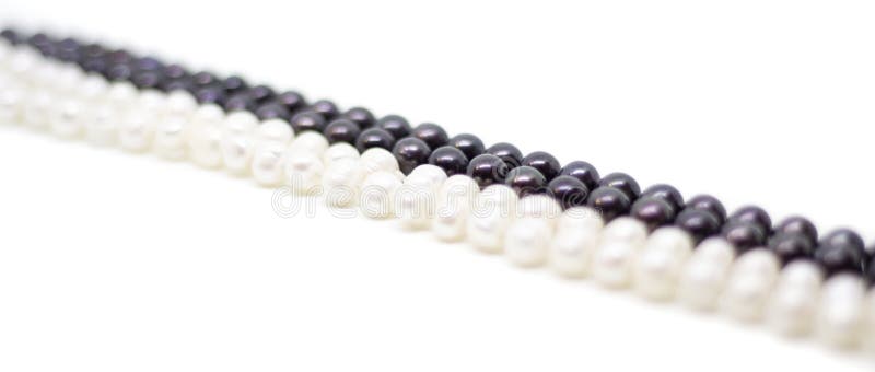 Two strands of white and black pearls intertwined on white background. Two strands of white baroque and black pearls intertwined on white background stock image