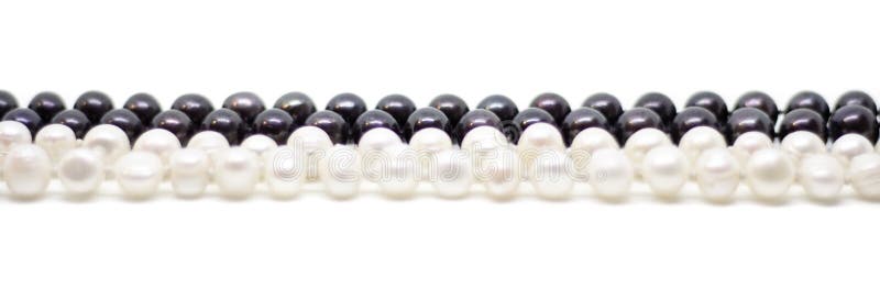 Two strands of white and black pearls intertwined on white background. Two strands of white baroque and black pearls intertwined on white background royalty free stock photo