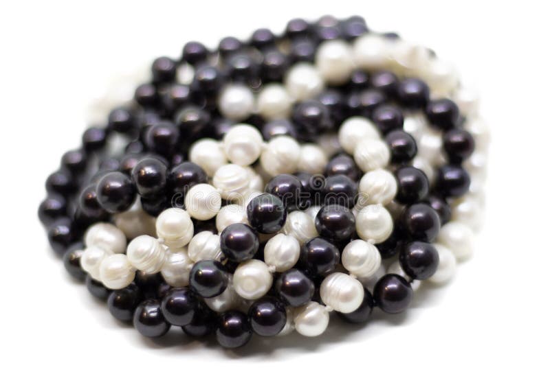 Two strands of white and black pearls intertwined on white background. Two strands of white baroque and black pearls intertwined on white background royalty free stock photography