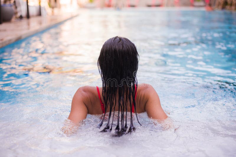 Woman with black hair lying back on the bassin rim of a swimming pool with rippled cool deep blue water.  royalty free stock image