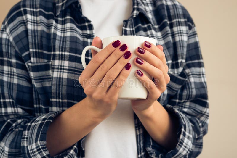 Woman with a burgundy manicure in plaid shirt holding white cup stock images