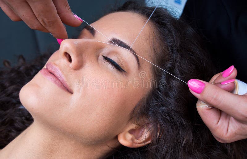 Woman on facial hair removal threading procedure. Attractive woman in beauty salon on facial hair removal eyebrow threading procedure stock photography